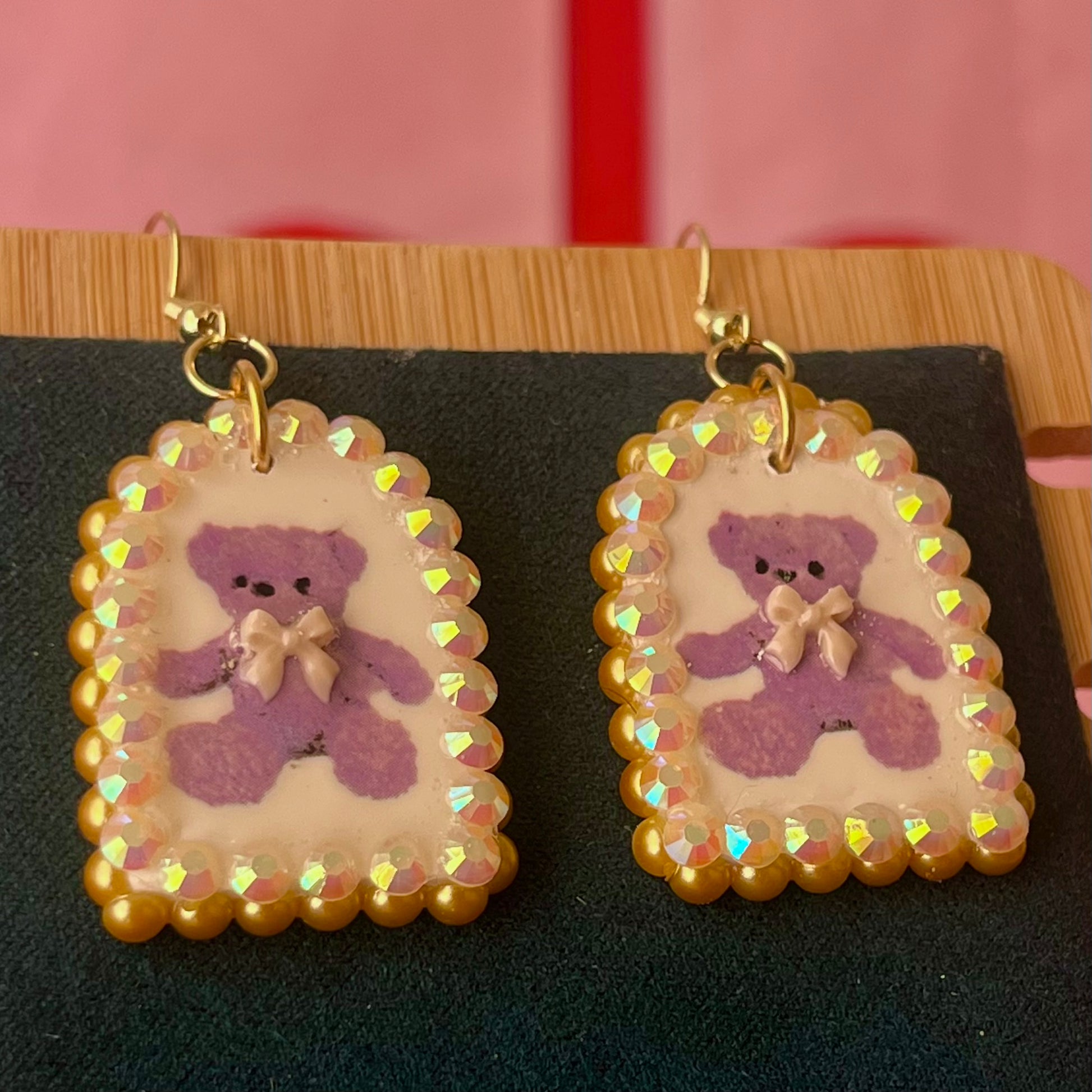 Handmade golden teddy bear bow charm earrings made from polymer clay with image transfer, featuring a 0.5‑inch arch charm framed by golden pearls and rhinestones, 18k gold‑plated hypoallergenic findings, luxuriously weighted, perfect teddycore, coquette, toycore, Y2K style statement piece.