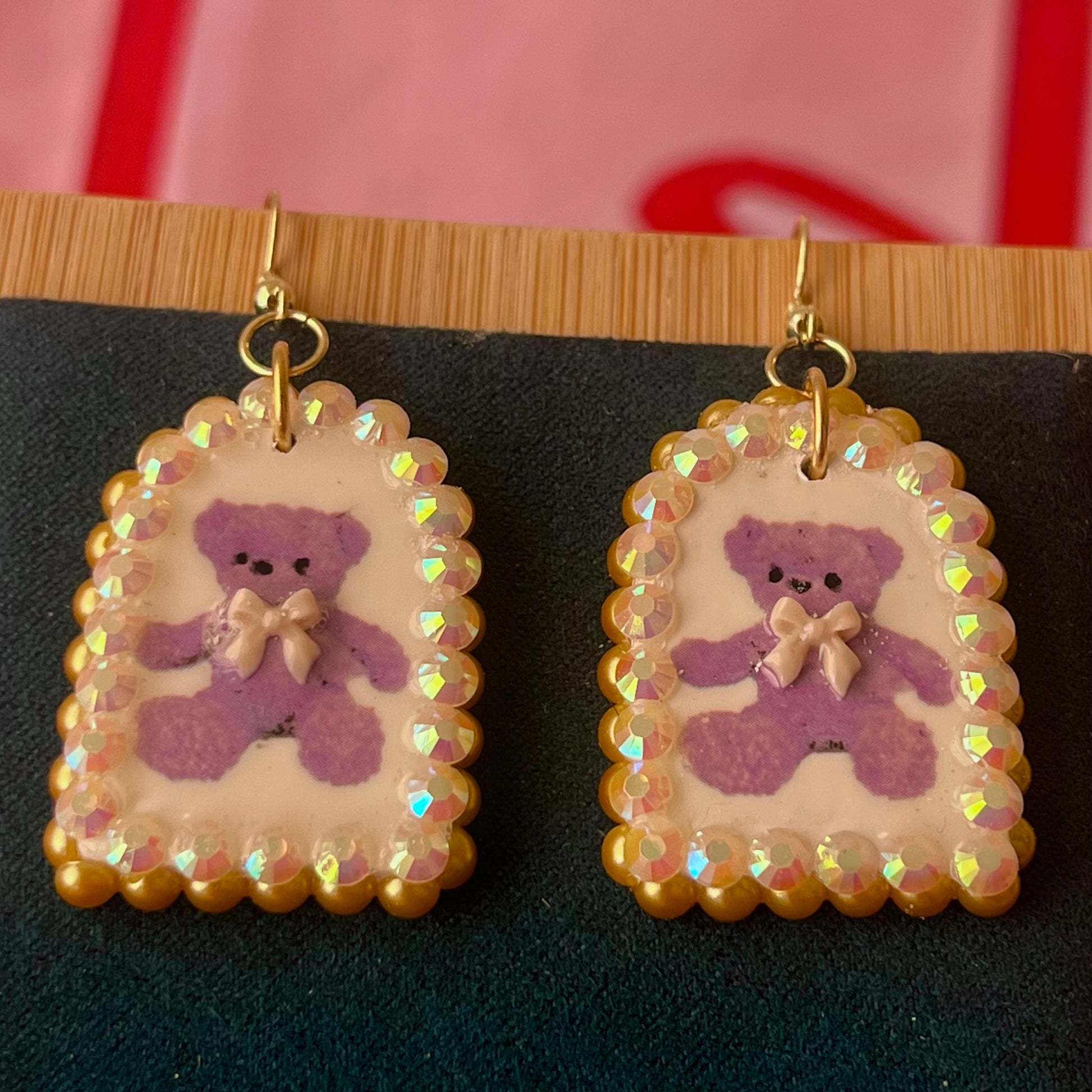 Handmade golden teddy bear bow charm earrings made from polymer clay with image transfer, featuring a 0.5‑inch arch charm framed by golden pearls and rhinestones, 18k gold‑plated hypoallergenic findings, luxuriously weighted, perfect teddycore, coquette, toycore, Y2K style statement piece.