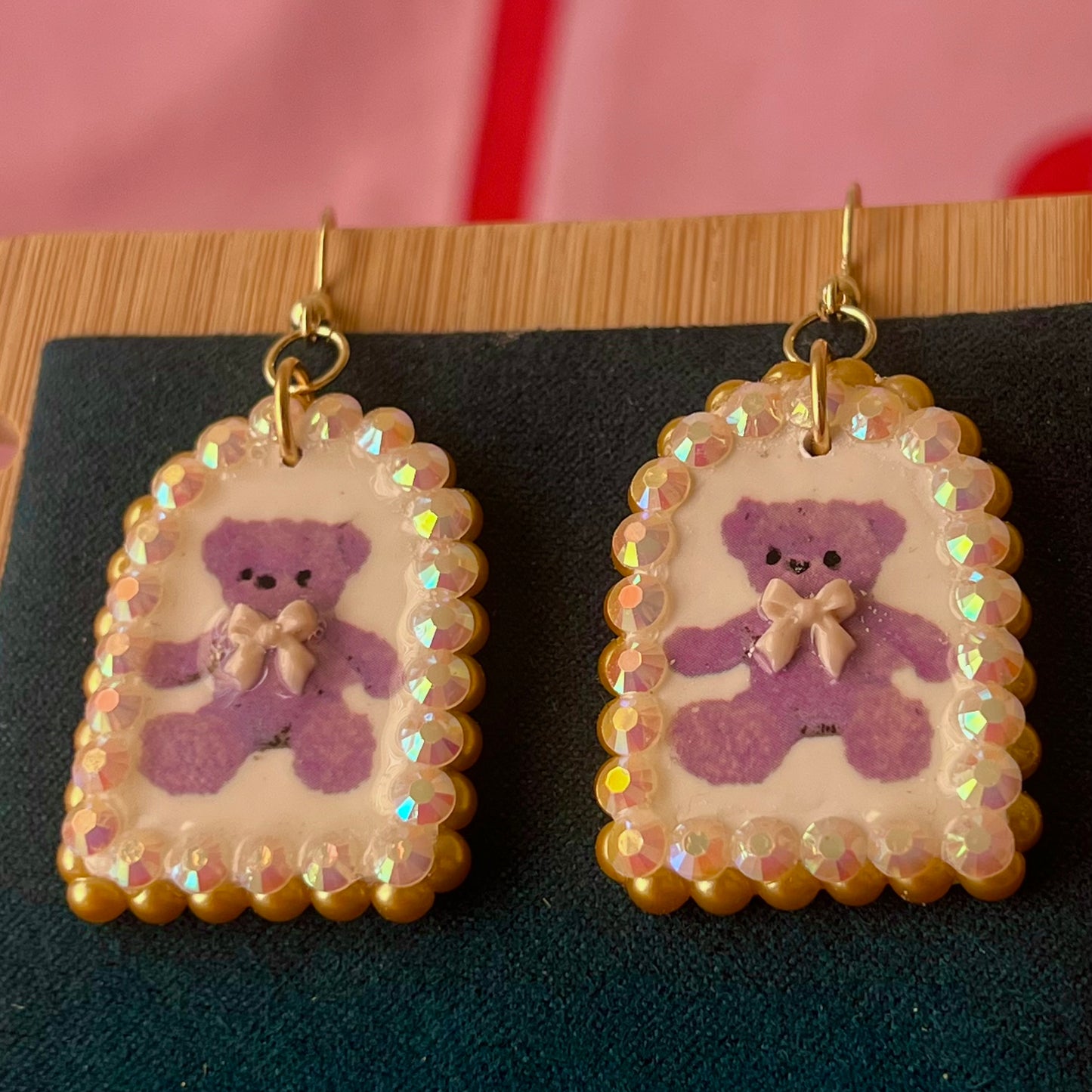 Handmade golden teddy bear bow charm earrings made from polymer clay with image transfer, featuring a 0.5‑inch arch charm framed by golden pearls and rhinestones, 18k gold‑plated hypoallergenic findings, luxuriously weighted, perfect teddycore, coquette, toycore, Y2K style statement piece.