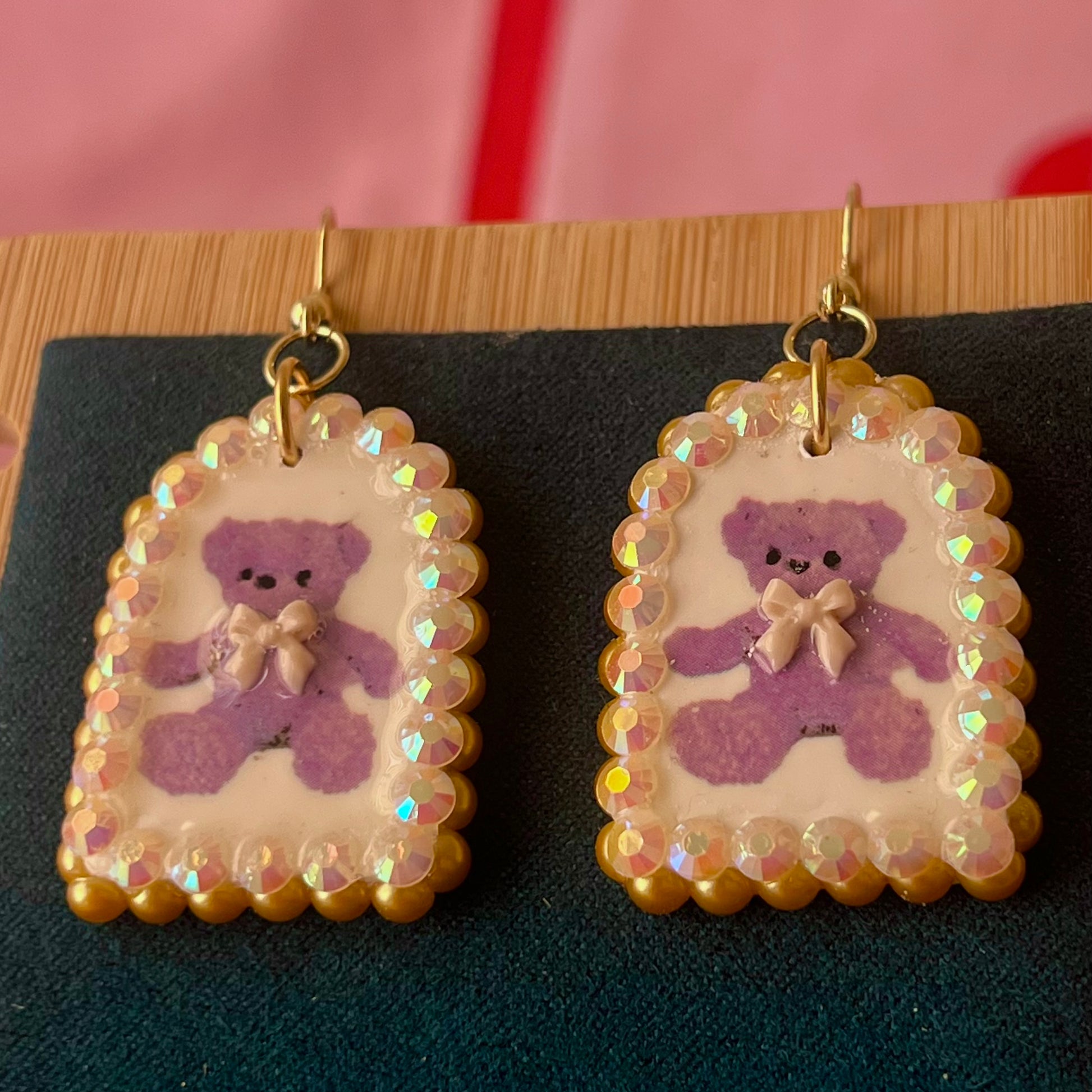Handmade golden teddy bear bow charm earrings made from polymer clay with image transfer, featuring a 0.5‑inch arch charm framed by golden pearls and rhinestones, 18k gold‑plated hypoallergenic findings, luxuriously weighted, perfect teddycore, coquette, toycore, Y2K style statement piece.