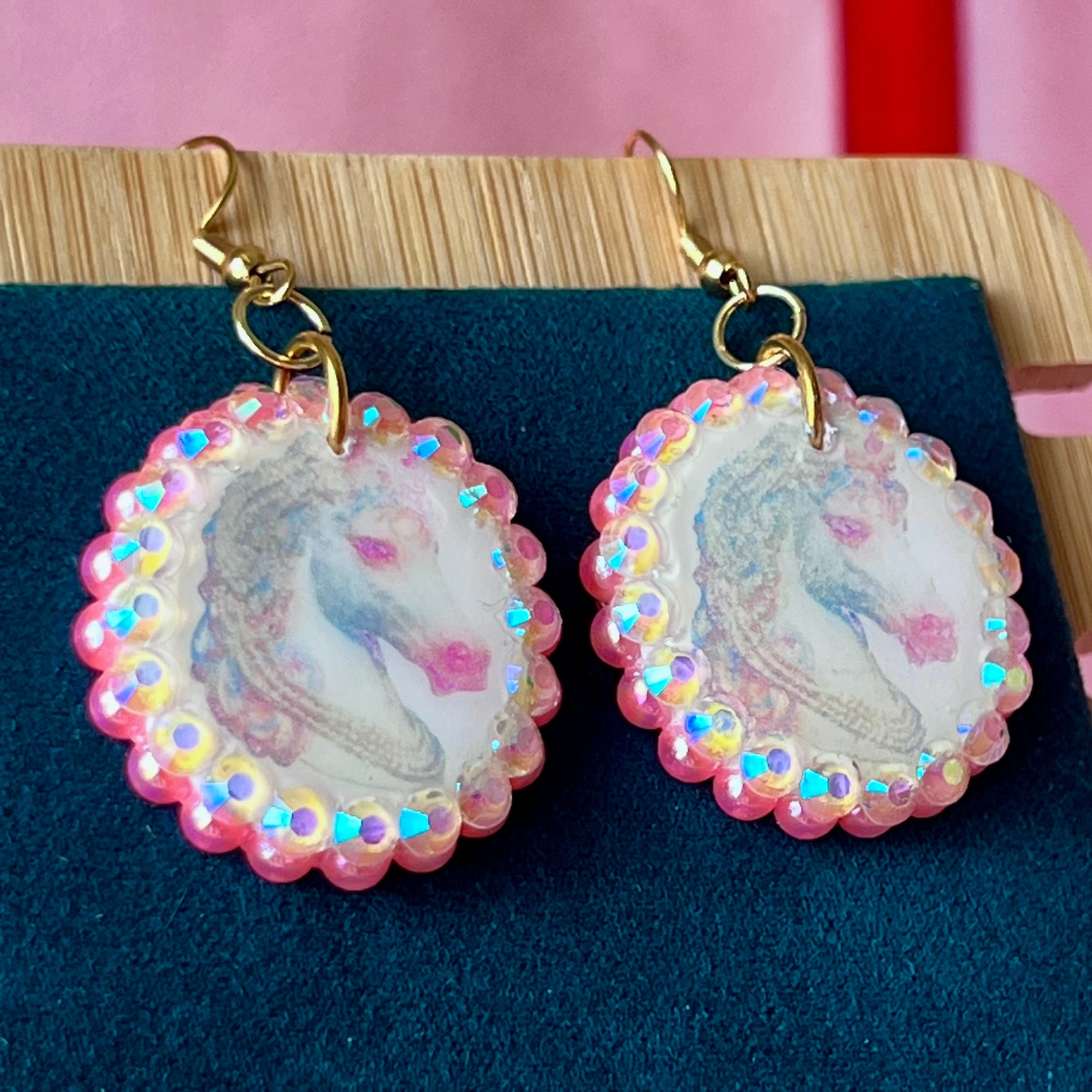 Alt text: "Handmade unicorn earrings featuring a pastel polymer‑clay charm with a soft fairy‑core unicorn, bedazzled by iridescent pink pearls and white gems, set in a gold‑plated fishhook finding; a whimsical, sparkly dangle earring perfect for Y2K, coquette, and pastel jewelry styles."