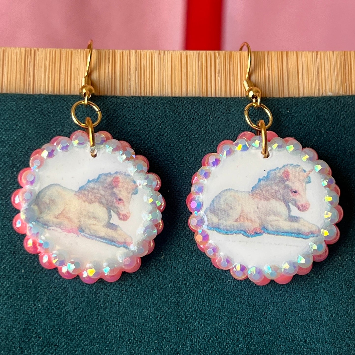Alt text: "Handmade unicorn earrings featuring a pastel polymer‑clay charm with a soft fairy‑core illustration, bedazzled by iridescent pink pearls and white gems, set in a gold‑plated fishhook finding; a whimsical, sparkly dangle earring perfect for Y2K, coquette, and pastel jewelry styles."