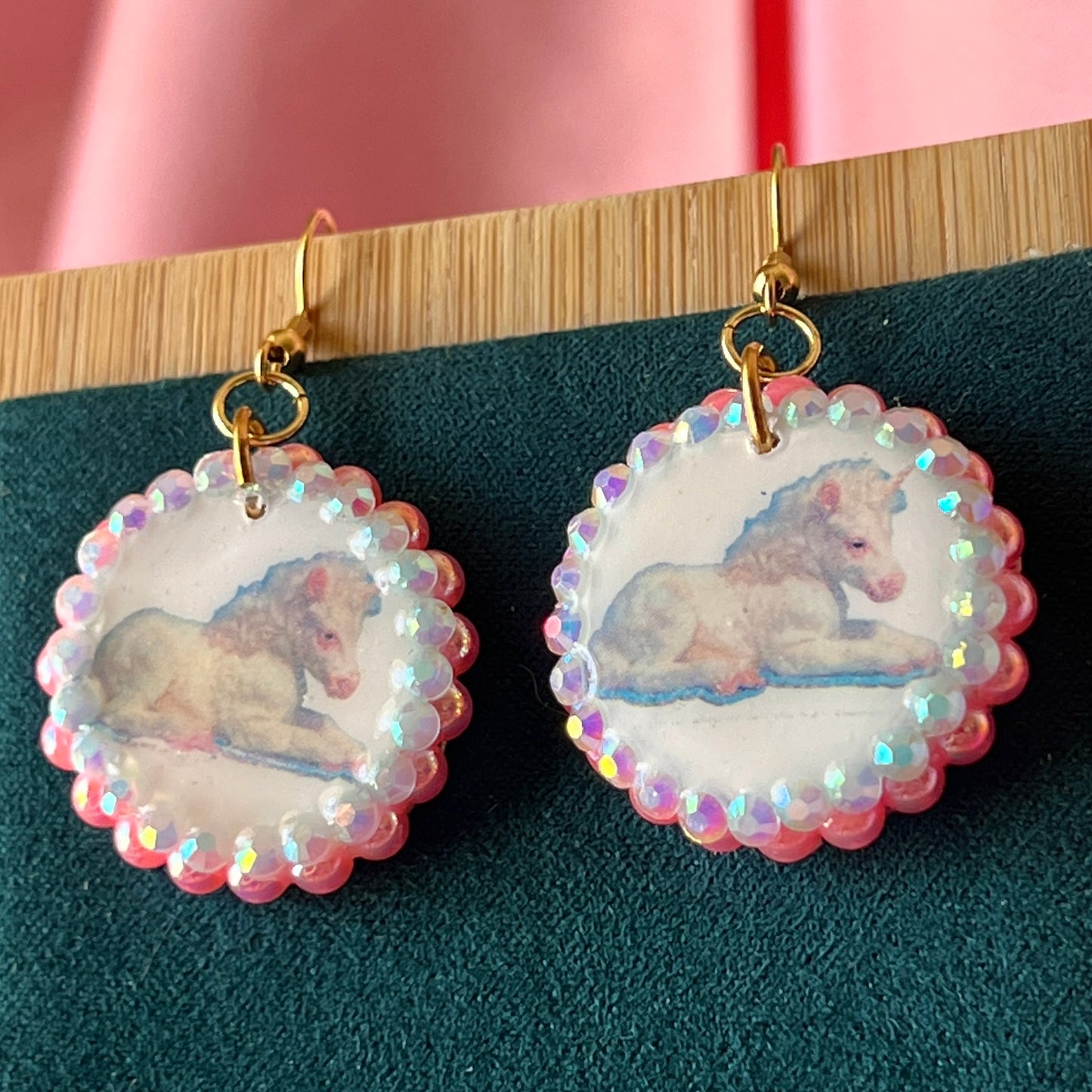 Alt text: "Handmade unicorn earrings featuring a pastel polymer‑clay charm with a soft fairy‑core unicorn, bedazzled by iridescent pink pearls and white gems, set in a gold‑plated fishhook finding; a whimsical, sparkly dangle earring perfect for Y2K, coquette, and pastel jewelry styles."