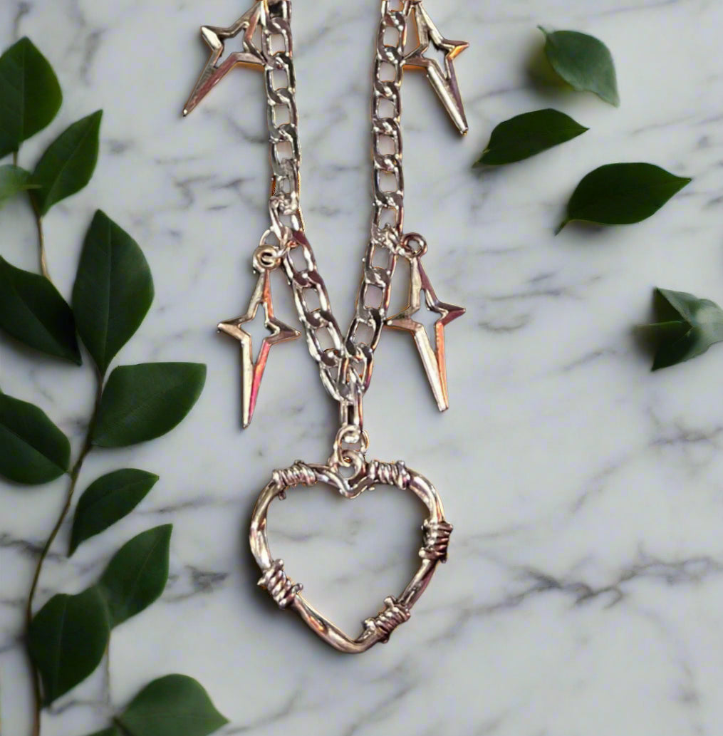 Necklace with heart and star pendants on a marble surface with green leaves