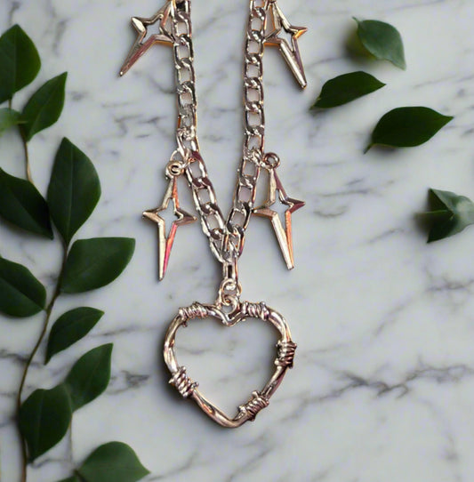 Necklace with heart and star pendants on a marble surface with green leaves