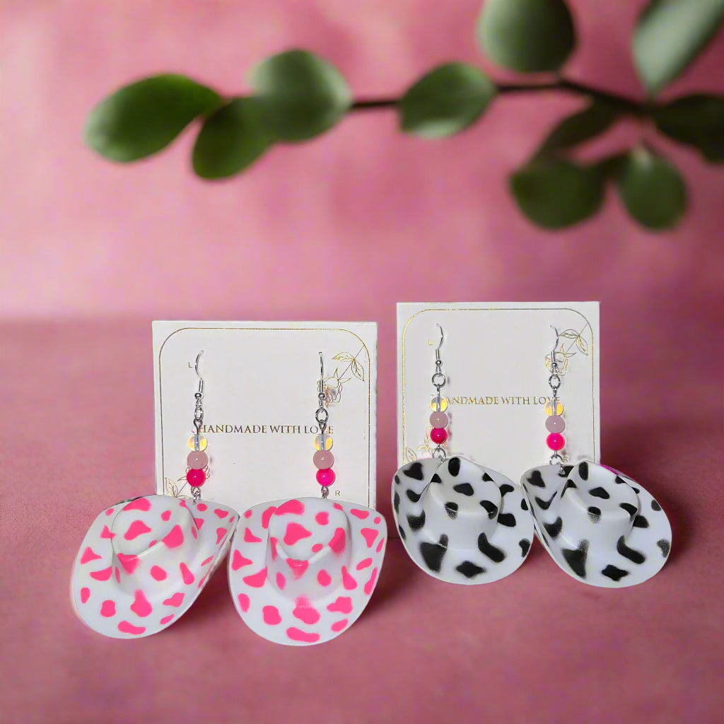 Two pairs of earrings on cards with a pink background and green leaves.