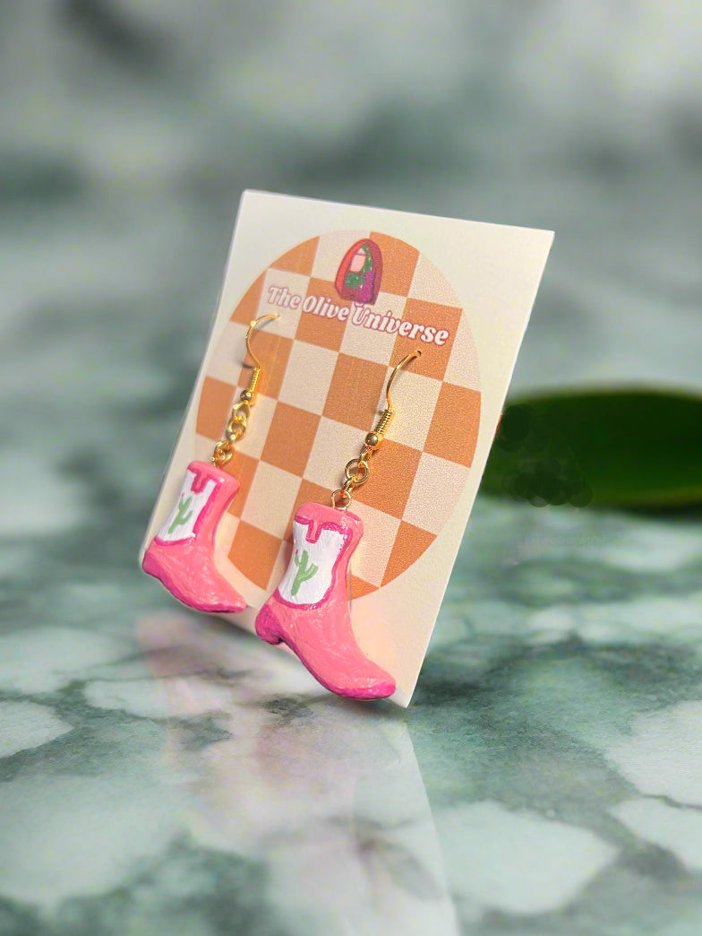 Pink rain boot earrings on a checkered card with 'The Nice Olive' branding, against a marble background.