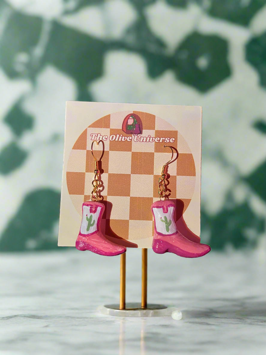 Pink earrings on a checkered card with 'The Home Universe' branding, against a dark background.