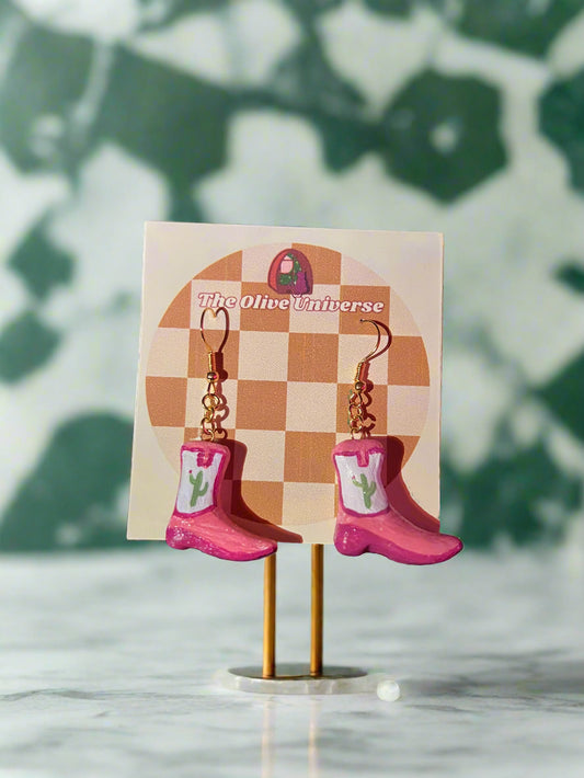 Pink earrings on a checkered card with 'The Home Universe' branding, against a dark background.