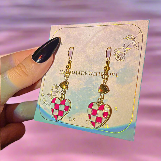 Heart-shaped earrings on a branded card with 'Hematite Hearts' text, held by a hand.