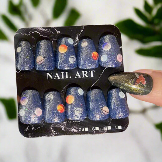 Space-themed nail art set with planets and stars on a blue glitter background, held by a person with matching nail design.