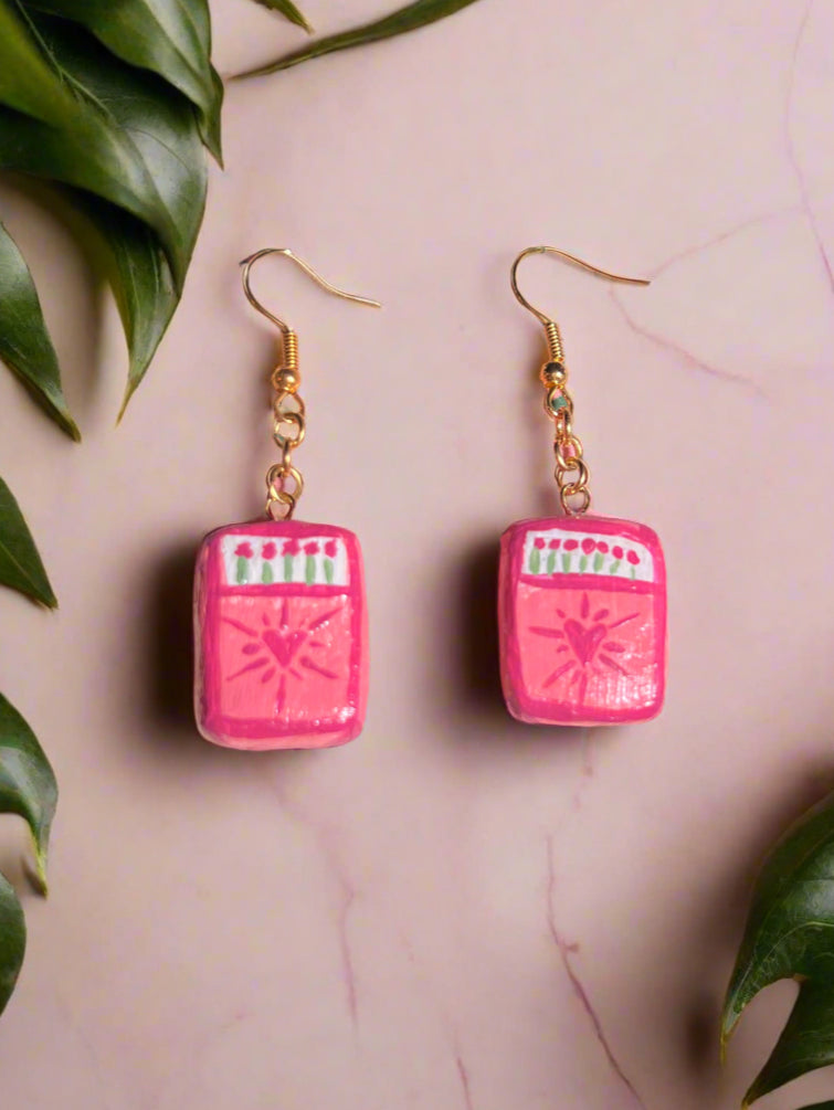 Pink earrings on a decorative card with a black background