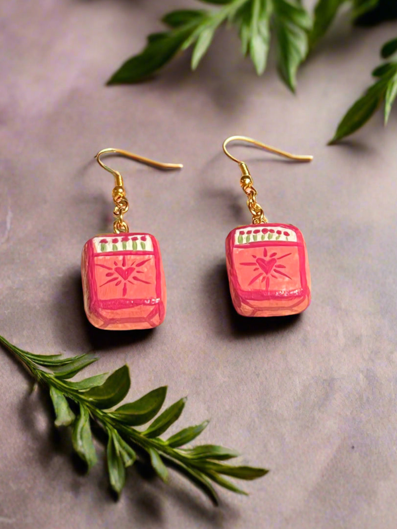 Pink earrings with gold hooks on a gray surface with green leaves.