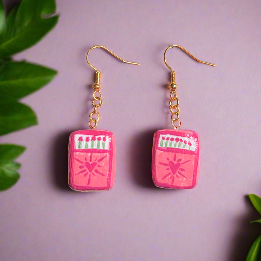 Pink rectangular earrings with gold hooks on a purple background