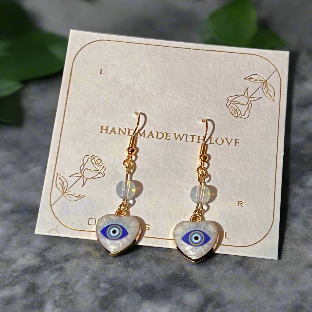 Heart-shaped earrings with eye design on a 'Handmade with Love' card.