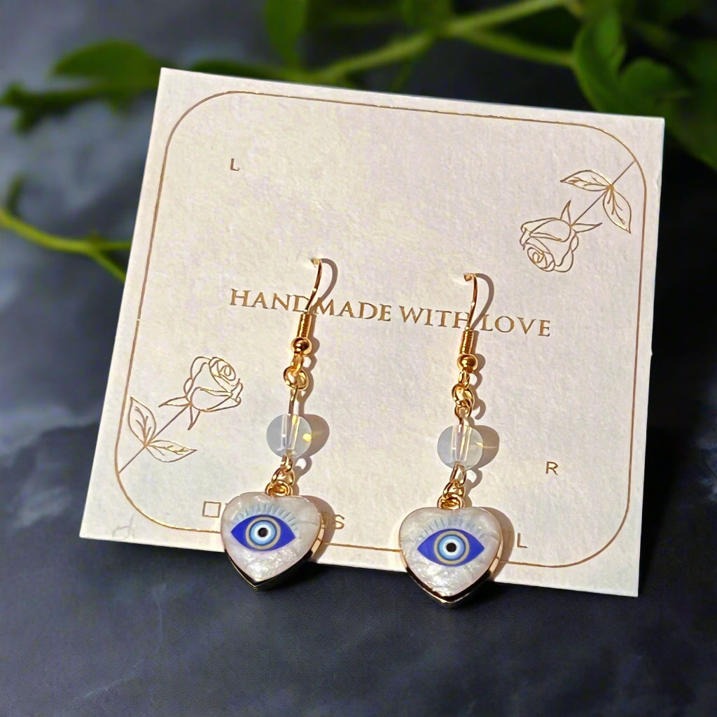 Heart-shaped earrings with eye design on a 'Handmade with Love' card.