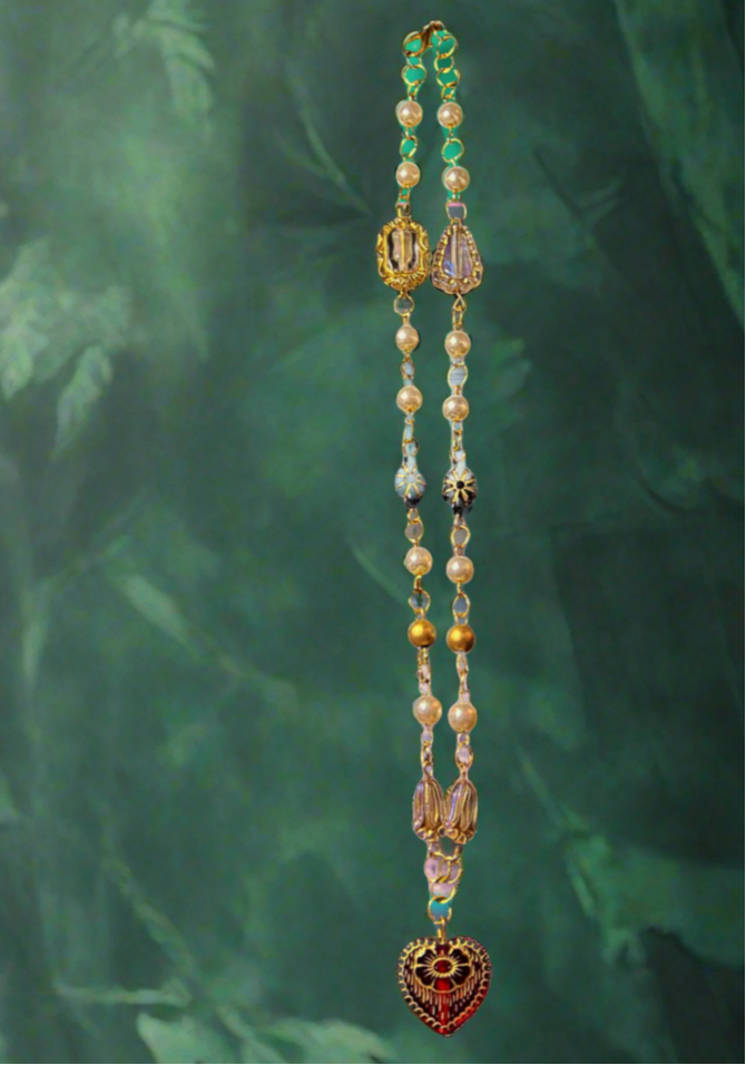 Beaded necklace with heart pendant on a beach setting, featuring 'Pirate Queen Of Hearts' and 'The Olive Universe'.