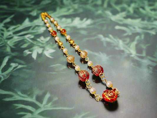 Necklace with pearls and red floral beads on a dark surface