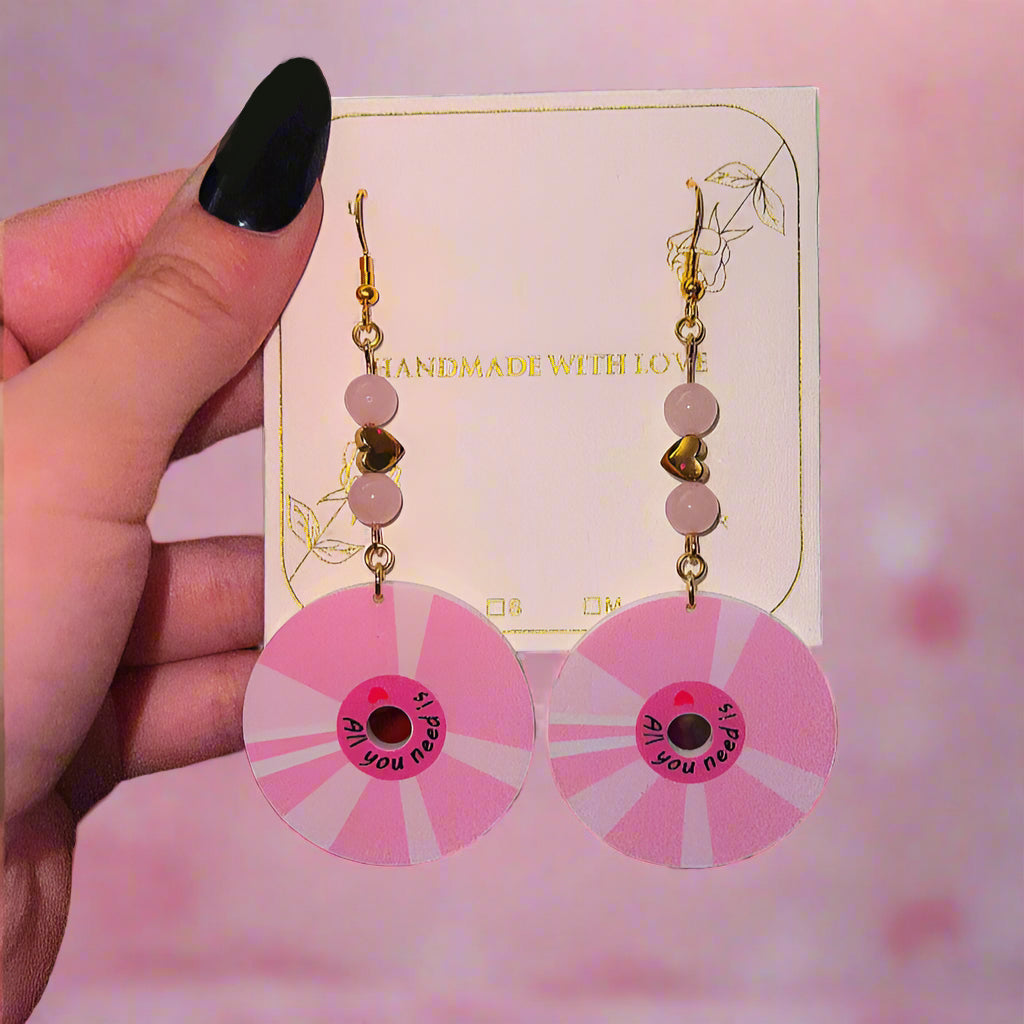 Pink circular earrings with a black center held by a hand on a blurred background.