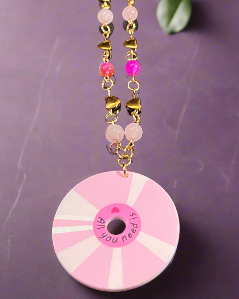 Pink and gold beaded necklace with a circular pendant on a dark background