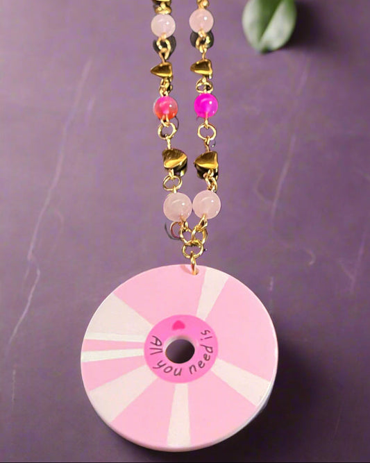 Pink and gold beaded necklace with a circular pendant on a dark background