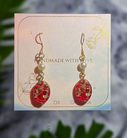 Red earrings with gold accents on a 'Handmade with Love' card against a blurred natural background