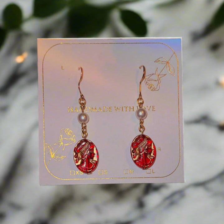Red and gold earrings on a card with a disco ball and candle in the background