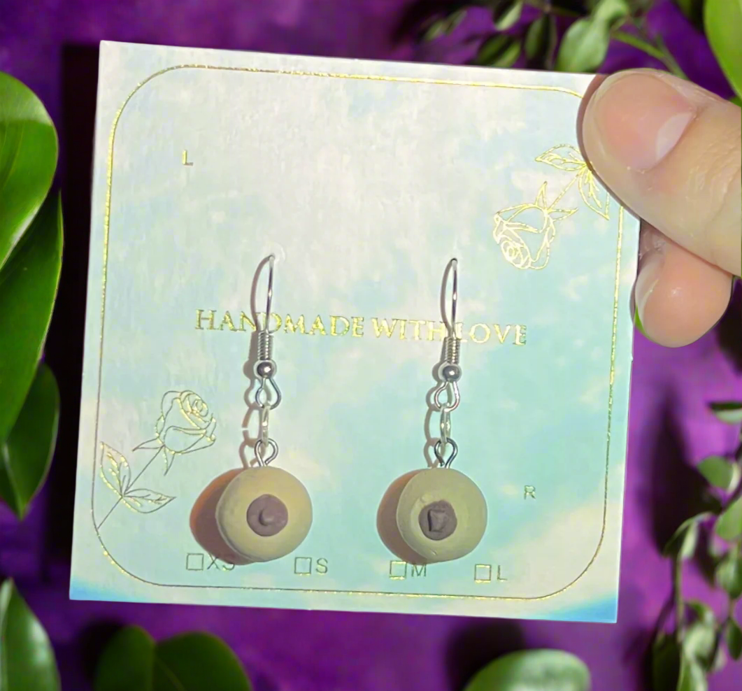Earrings on a card with 'Handmade with Love' text, held by a hand against a colorful background.