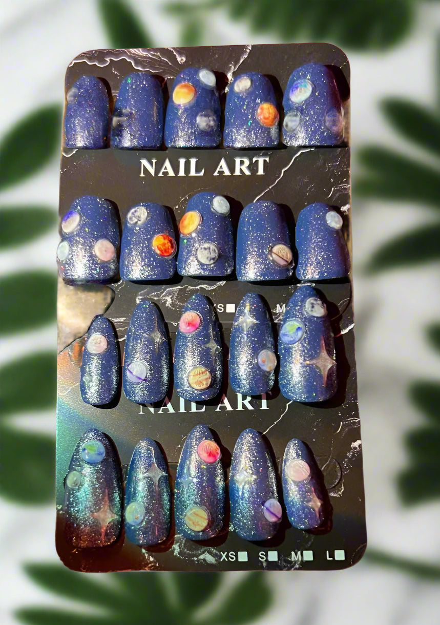 Nail art set with space-themed design on a black card, held by a hand with matching nail color.