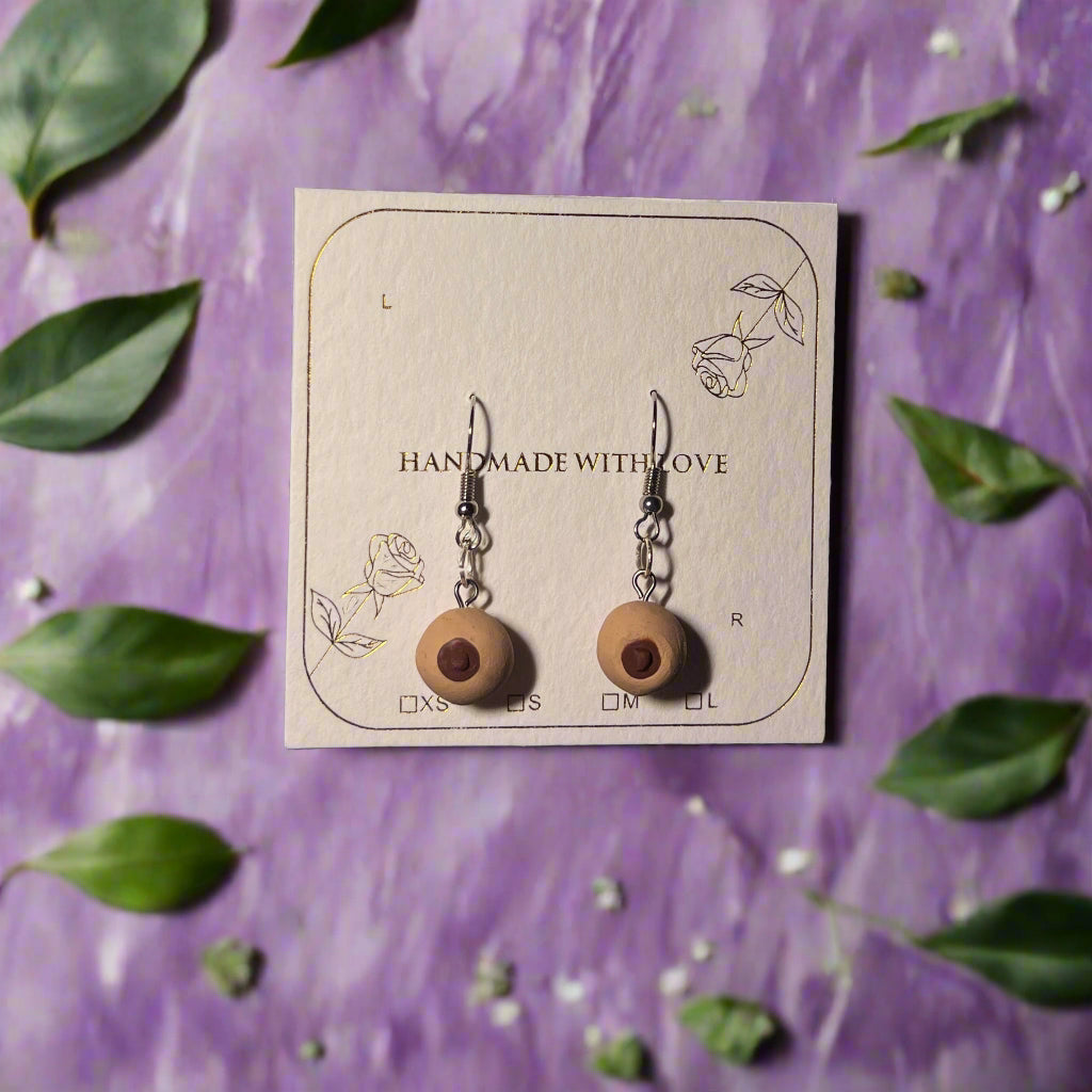 Wooden earrings on a card with 'Handmade with Love' text, surrounded by green leaves on a purple background
