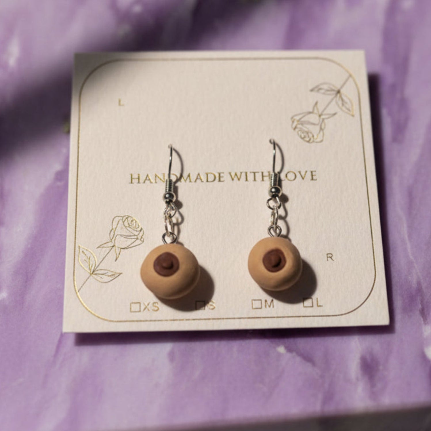 Wooden earrings on a card with 'Handmade with Love' text, surrounded by green leaves on a purple background